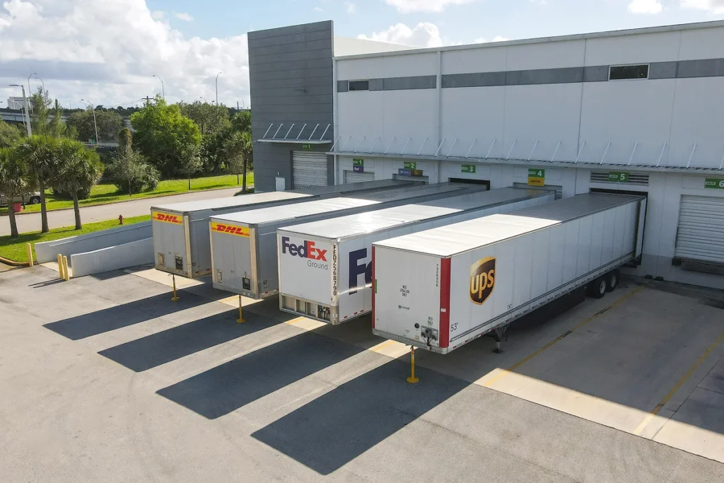 As I strolled through the bustling hub of activity at the loading docks, I couldn’t help but feel a sense of admiration for the scene before me—a trifecta of industry giants, DHL, FedEx, and UPS, poised like thoroughbreds at a starting gate. The semi-trailers stood ready to sprint across our vast nation under a sky dotted with wisps of clouds and framed by majestic trees swaying gently in the breeze. In this picturesque setting reminiscent of a cinematic moment (you can almost hear your favorite Spielberg score playing), each trailer embodies an integral piece of the dynamic carrier network that effortlessly connects products with people. This is not just logistics; its storytelling on wheels! Amongst nature’s splendor meeting human ingenuity, it’s easy to see how ShipMonk.com choreographs such seamless partnerships. Efficiency wrapped in reliability—its Captain Phillips meets Marthas perfect party planning! There you have it: distribution impeccably aligned to meet every need from sea to shining sea. via ShipMonk.com