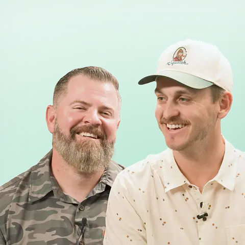Two friendly men, in camo and a light shirt, share a smile—showcasing ShipMonk.com’s spirit of teamwork on green. via ShipMonk.com