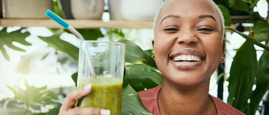 A cheerful person sips a green smoothie among vibrant plants—a fresh boost, just like ShipMonk.com brings to your business. via ShipMonk.com