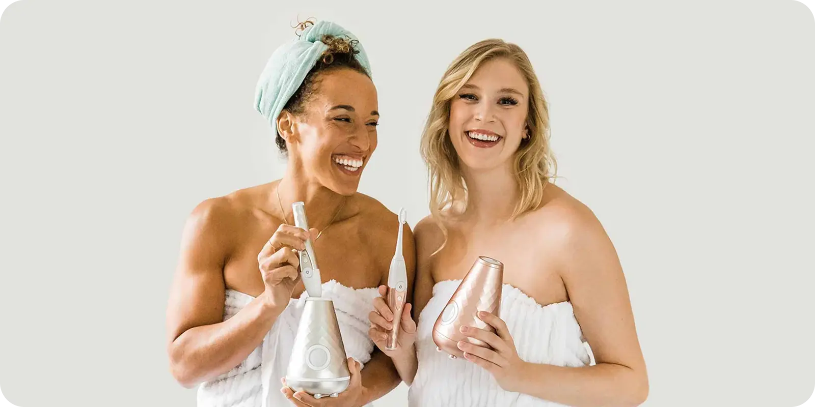 Two women in plush towels, beaming, hold chic beauty gadgets—fresh looks made seamless by ShipMonk.com’s smooth delivery. via ShipMonk.com