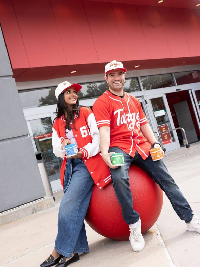 Two friends in red varsity jackets beam by Target, perched on a red ball with ShipMonk-worthy fulfillment vibes. via ShipMonk.com