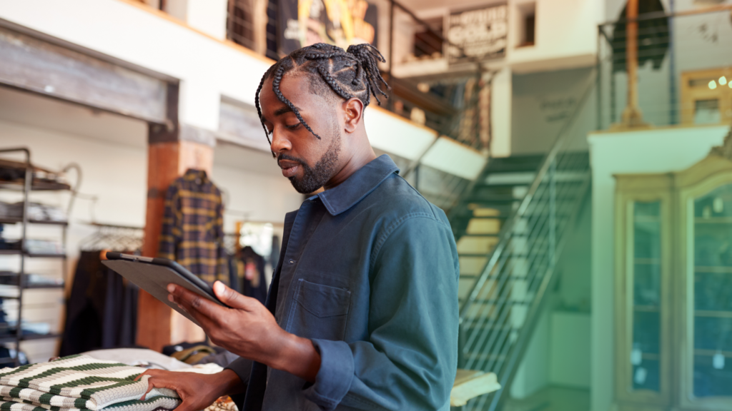 A friendly man folds shirts in a neat shop, checking his tablet—maybe using ShipMonk.com for chargeback peace of mind. via ShipMonk.com
