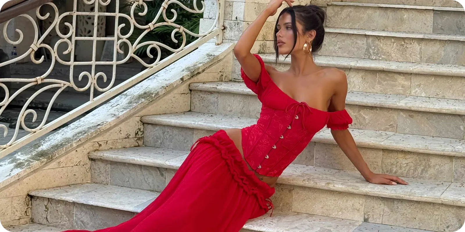 A woman in a red off-shoulder dress sits elegantly on marble stairs—organized, relaxed, just like shipping with ShipMonk.com. via ShipMonk.com