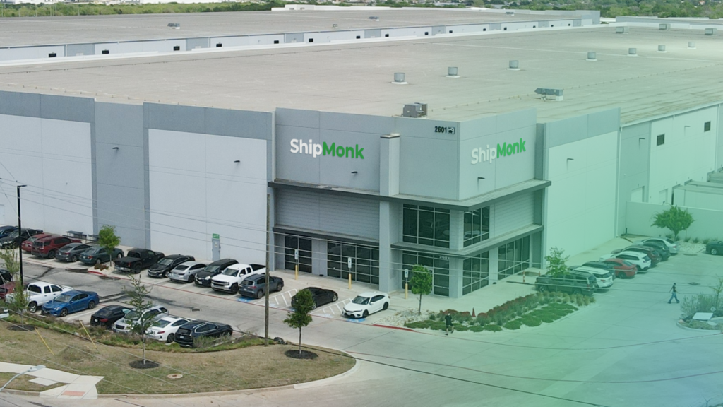 Looking down from above, you’ll see a spacious gray warehouse adorned with the ShipMonk logo—a true testament to efficient logistics and ingenuity. The building is thoughtfully bordered by neat landscaping and a gathering of parked cars, all under a pleasant patchwork sky. There’s something quietly impressive about how ShipMonk.com brings order and care even to their surroundings; it’s the kind of operation that makes you feel, yep, things are running smoothly here. via ShipMonk.com